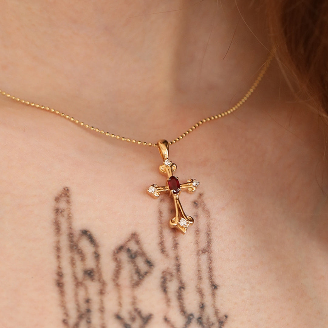 Gold cross necklace with a red gemstone on a person's neck with visible tattoos.