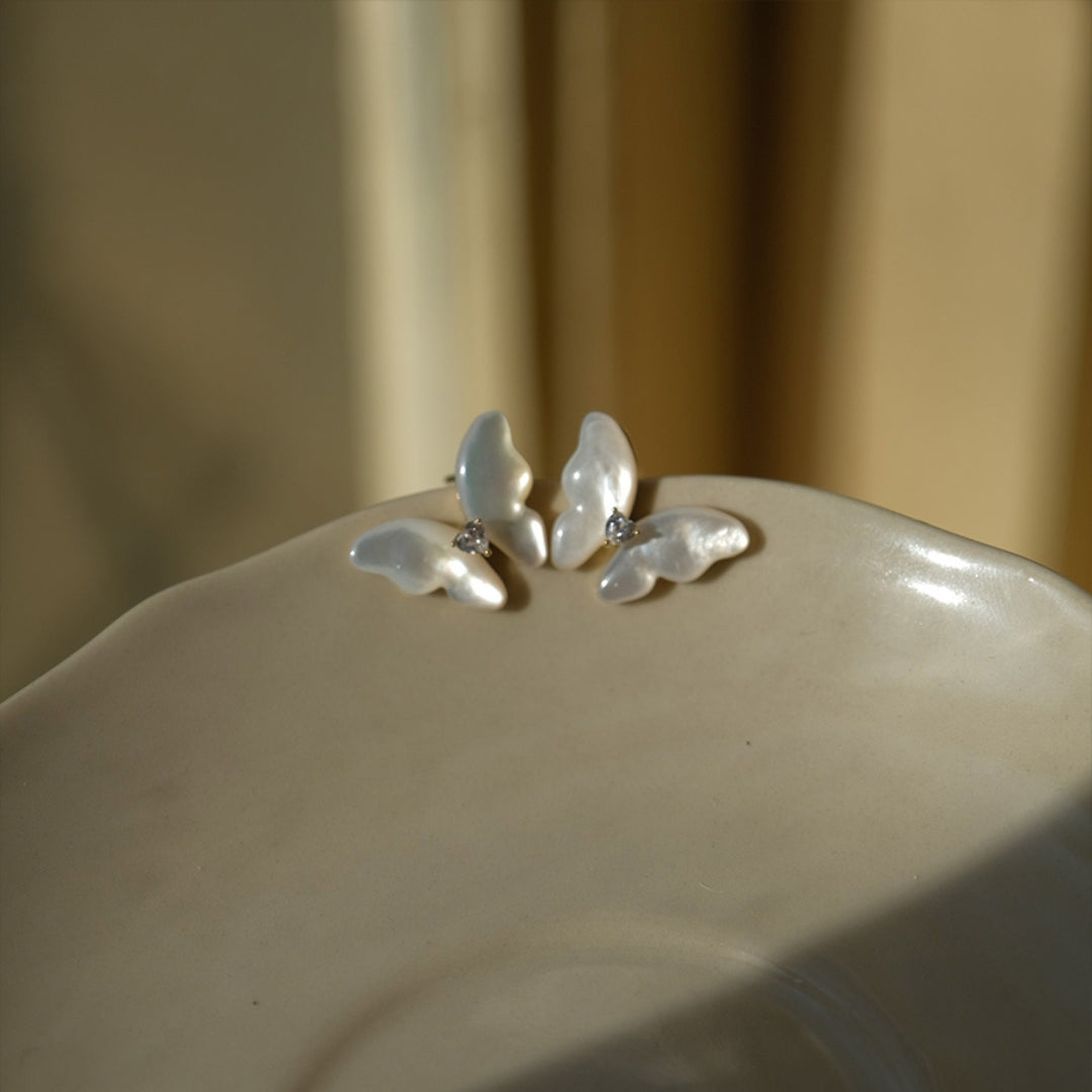 Pearl butterfly earrings on a beige ceramic dish with a neutral background