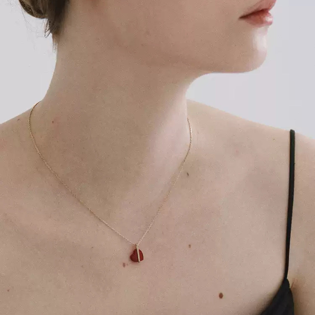 Necklace with a red heart pendant worn by a person on a neutral background