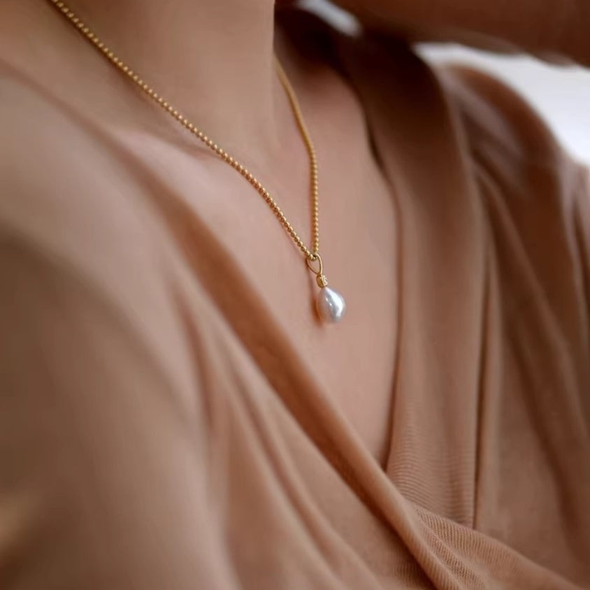 Detail shot of lustrous white teardrop pearl pendants hanging from delicate gold ball chains, showing the organic baroque shape. 4