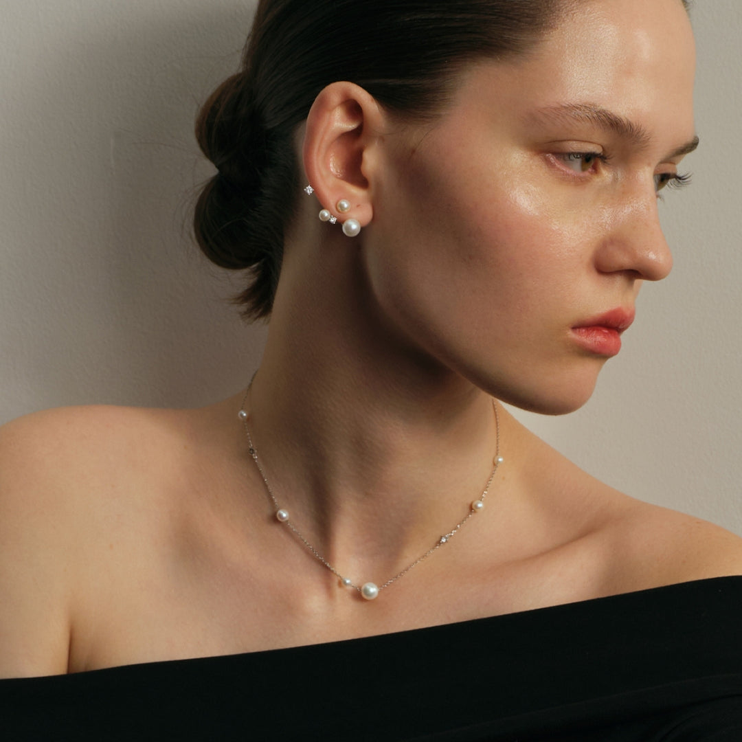 Woman wearing pearl and diamond earrings and a cultured freshwater pearl necklace against a neutral background.