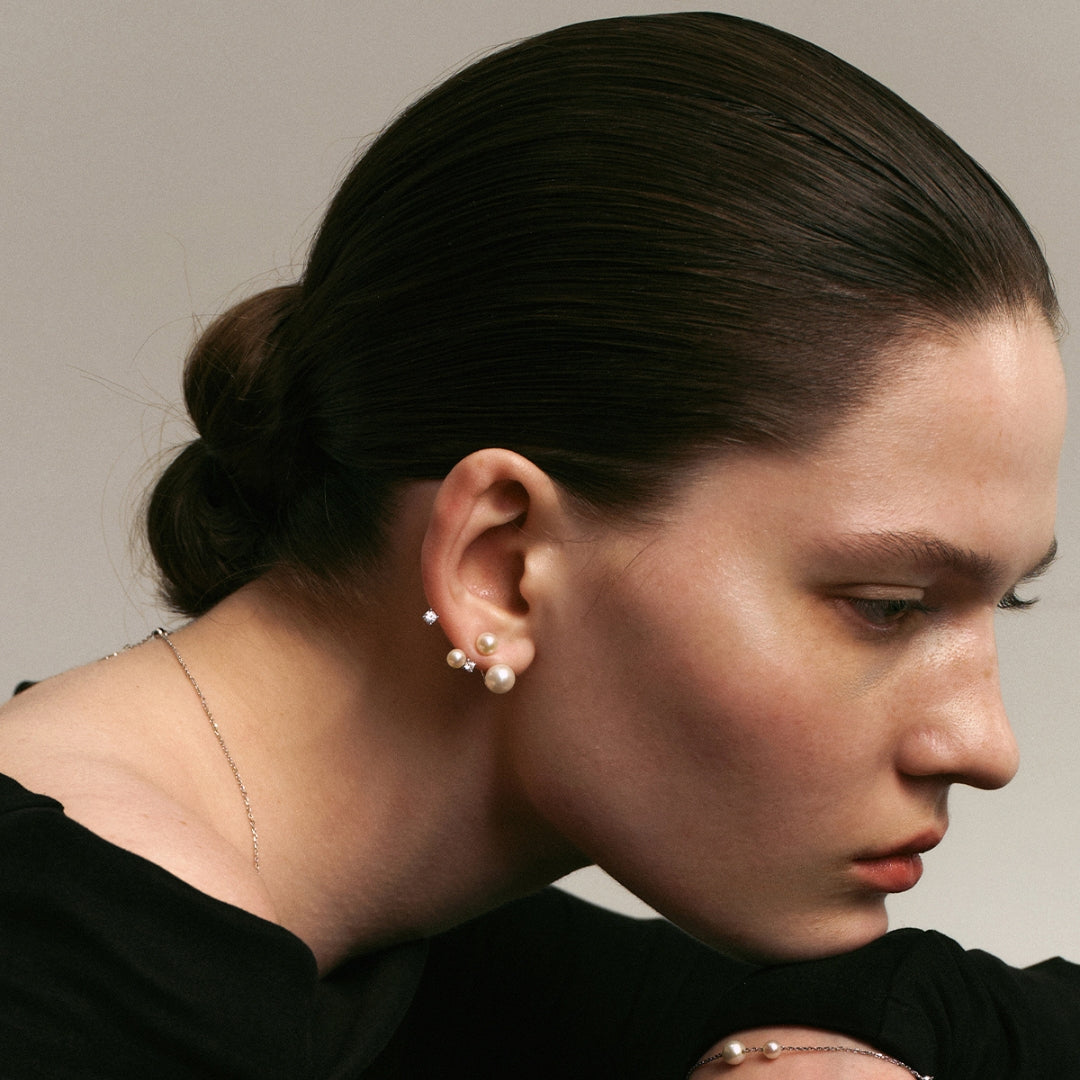 Close-up of a person wearing pearl and diamond earrings with a neutral background