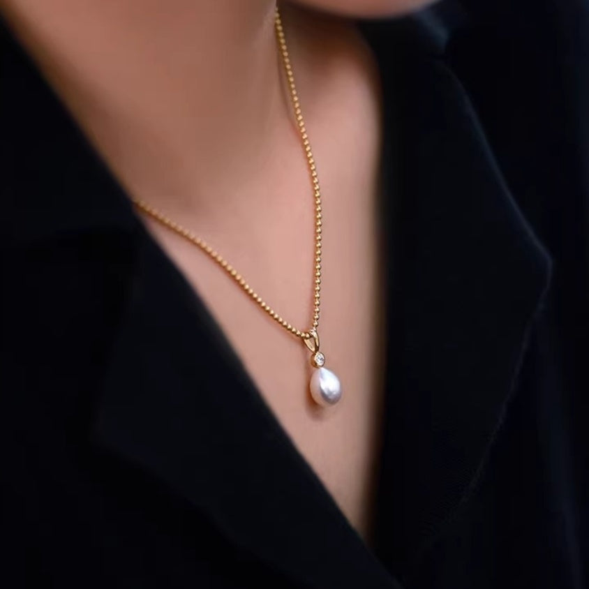 Detail shot of lustrous white teardrop pearl pendants hanging from delicate gold ball chains, showing the organic baroque shape. 2