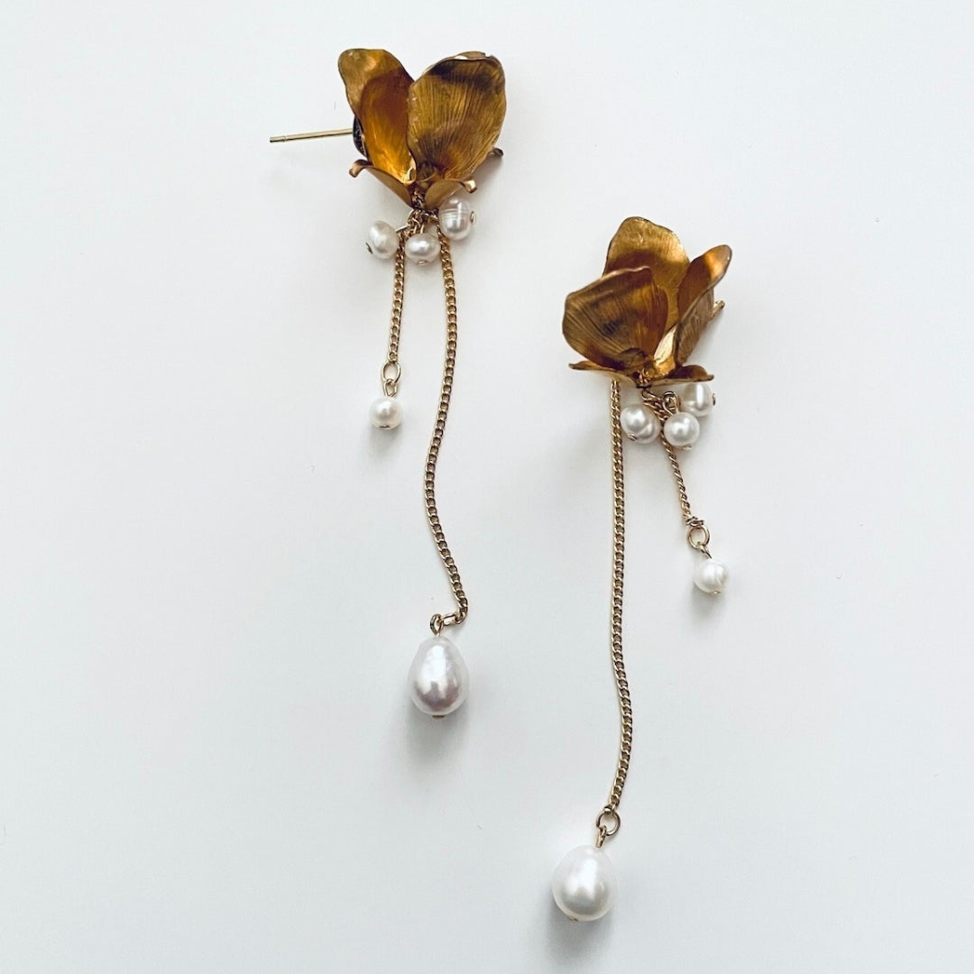 Gold floral earrings with pearl drops on a white background