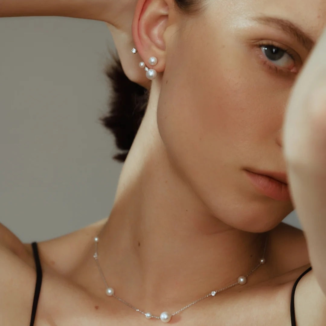 Close-up of a person wearing freshwater pearl earrings and a pearl necklace against a neutral background