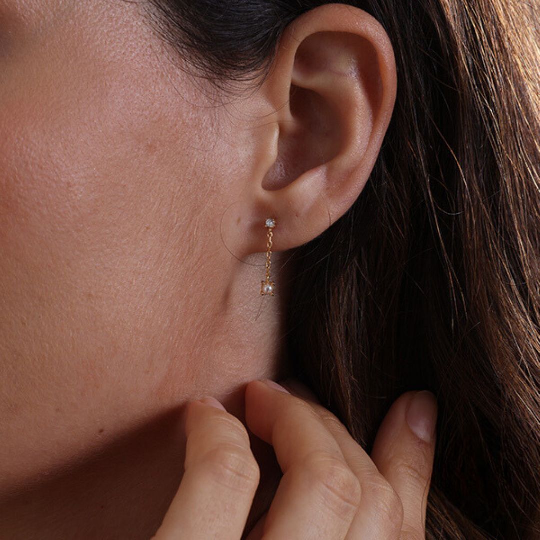 Close-up of tiny pearl and diamond short chain earrings in gold, featuring natural freshwater pearls and diamonds; elegant bridal jewelery or daily wear.