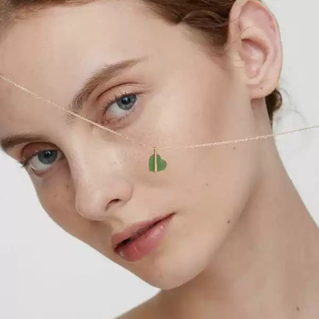 Close-up of a woman wearing a delicate 14k gold necklace with a green heart pendant.