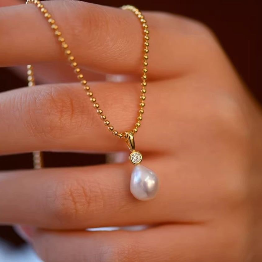 Detail shot of lustrous white teardrop pearl pendants hanging from delicate gold ball chains, showing the organic baroque shape. 1