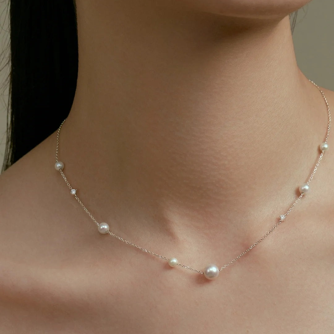 Diamond and pearl necklace on a person's neck against a neutral background