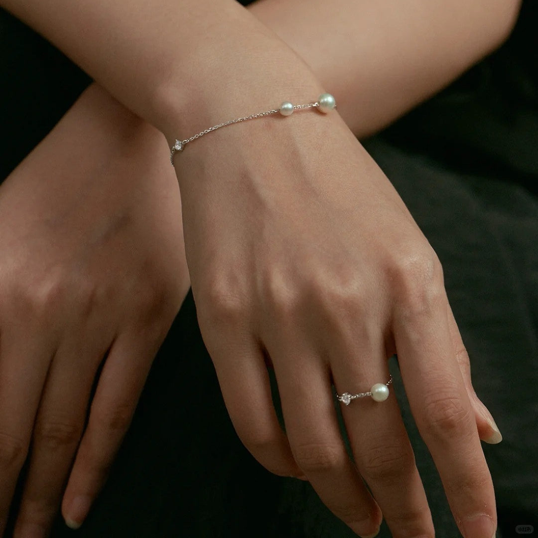 Close-up of hands wearing pearl bracelet and silver chain ring on a dark background