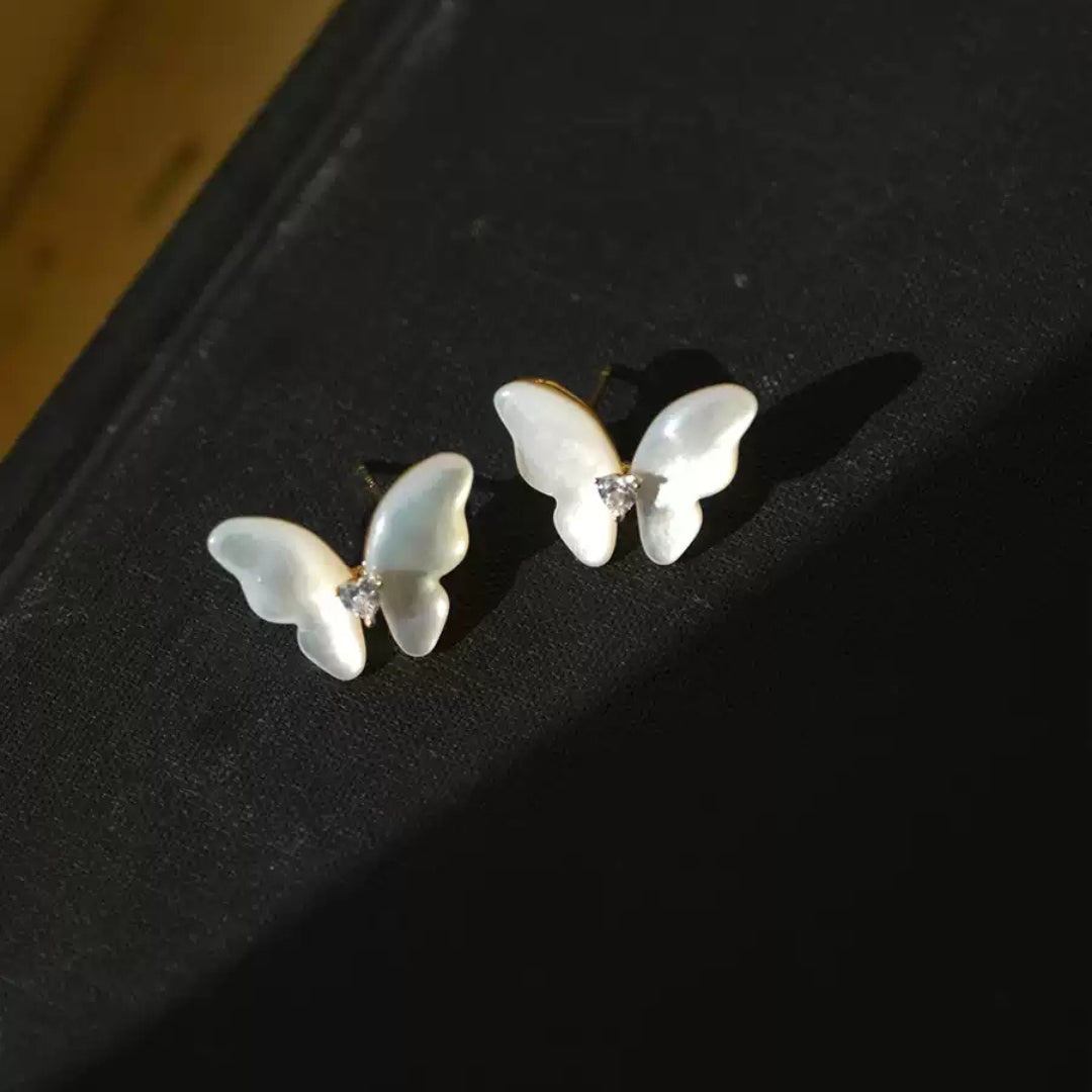 Butterfly-shaped pearl earrings on a dark surface