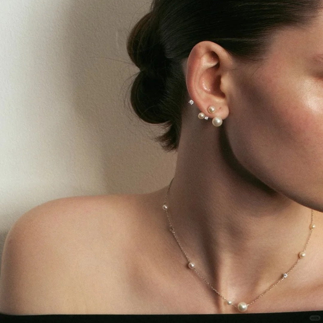 Close-up of a person wearing celestial pearl diamond earrings and a pearl necklace against a neutral background