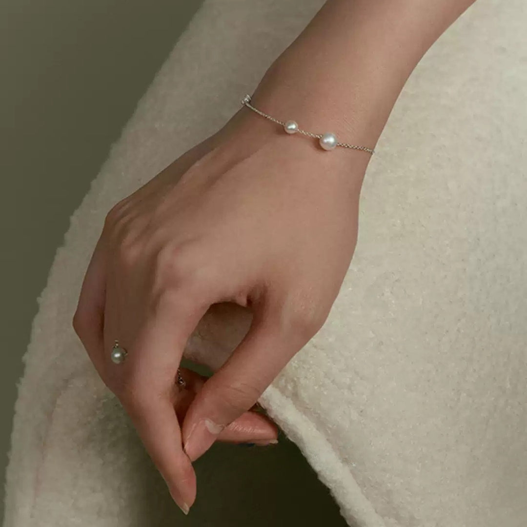 Hand wearing a freshwater pearl bracelet on a neutral background