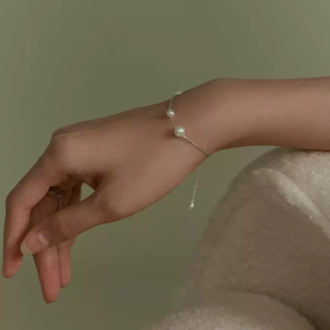 Hand wearing a delicate silver diamond pearl bracelet against a neutral background