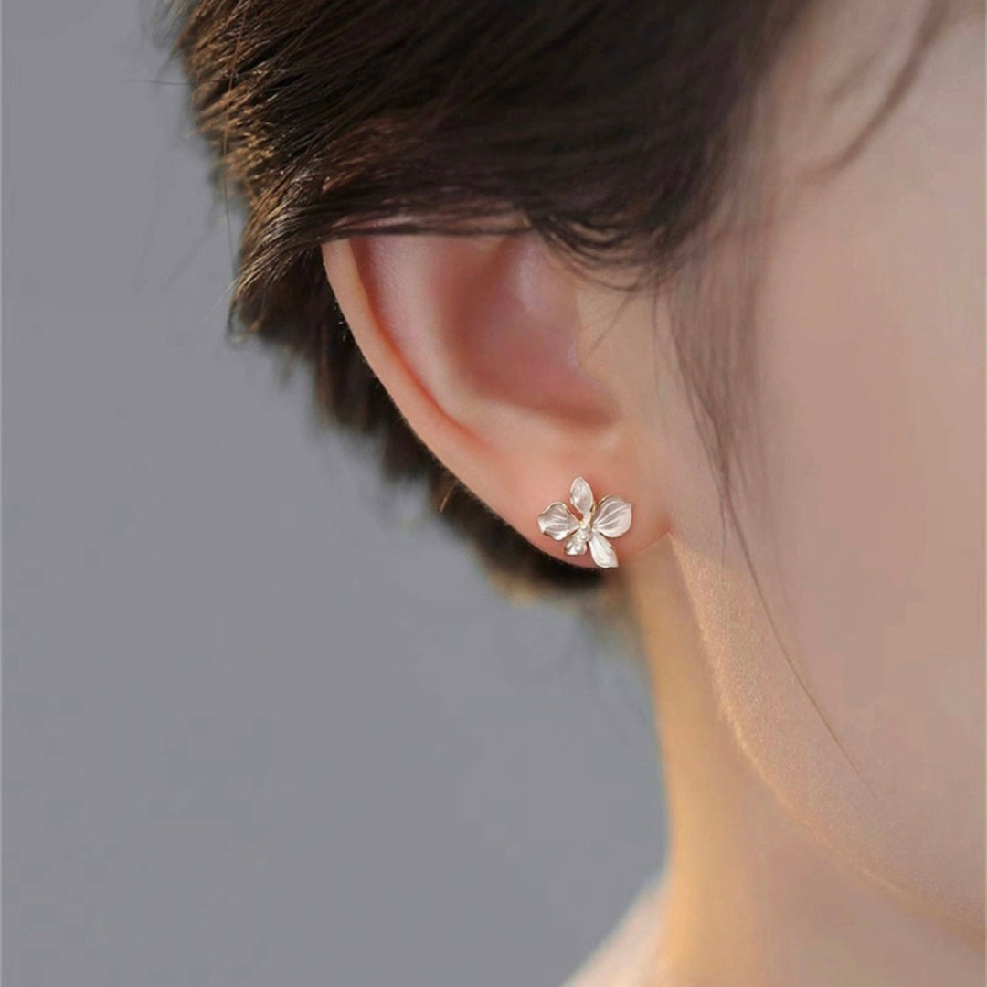 Silver flower earring worn by a person with a neutral background