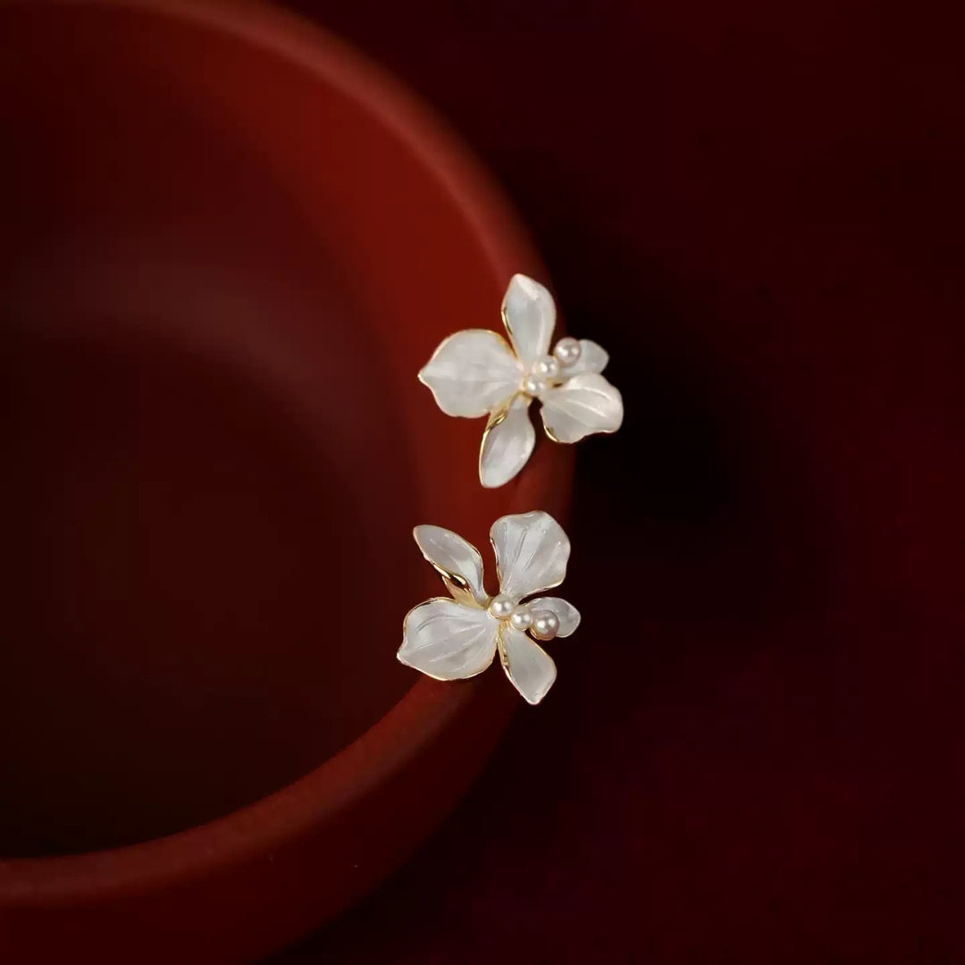 White flower earrings with pearl centers on a dark red background