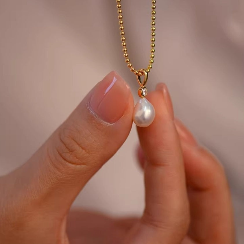 Detail shot of lustrous white teardrop pearl pendants hanging from delicate gold ball chains, showing the organic baroque shape. 6