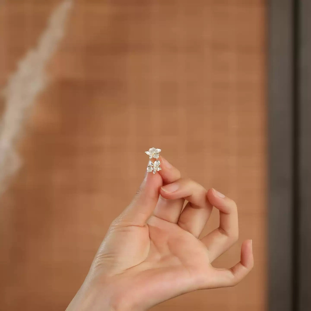 Hand holding a pair of white flower earrings against a blurred background