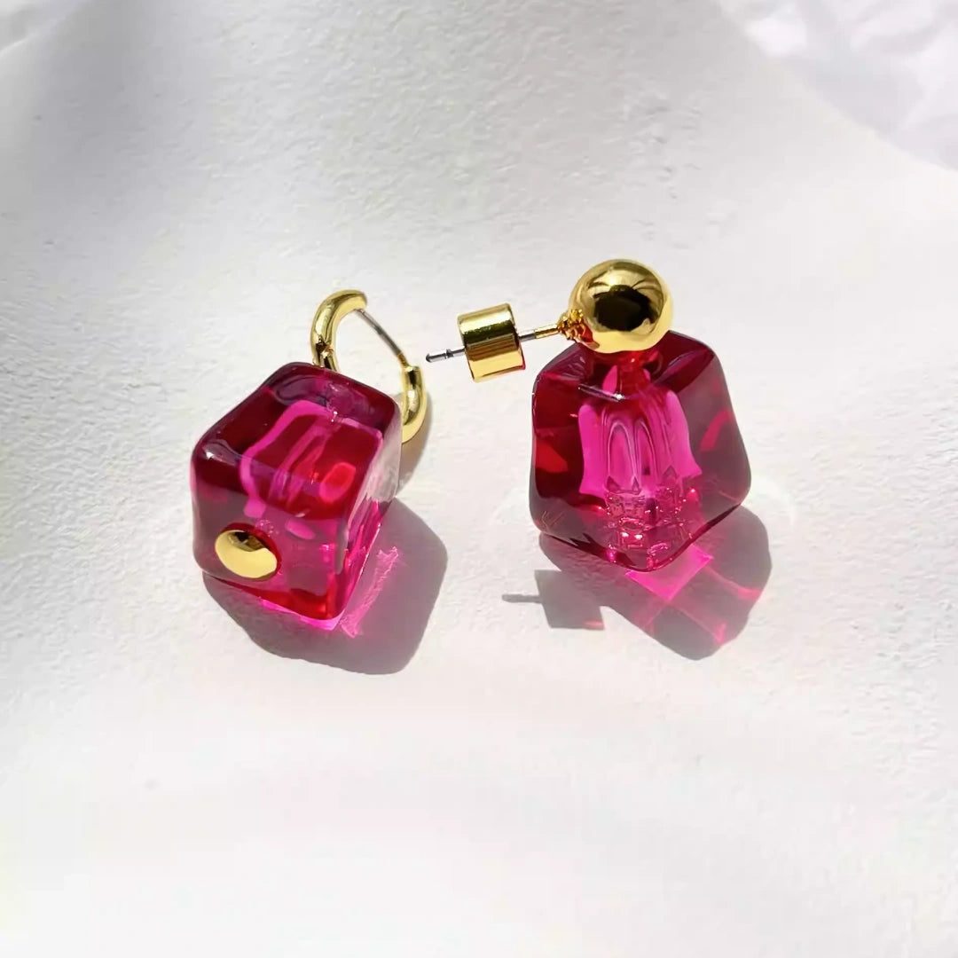 Flatlay of vibrant pink glass earrings on a white textured background.