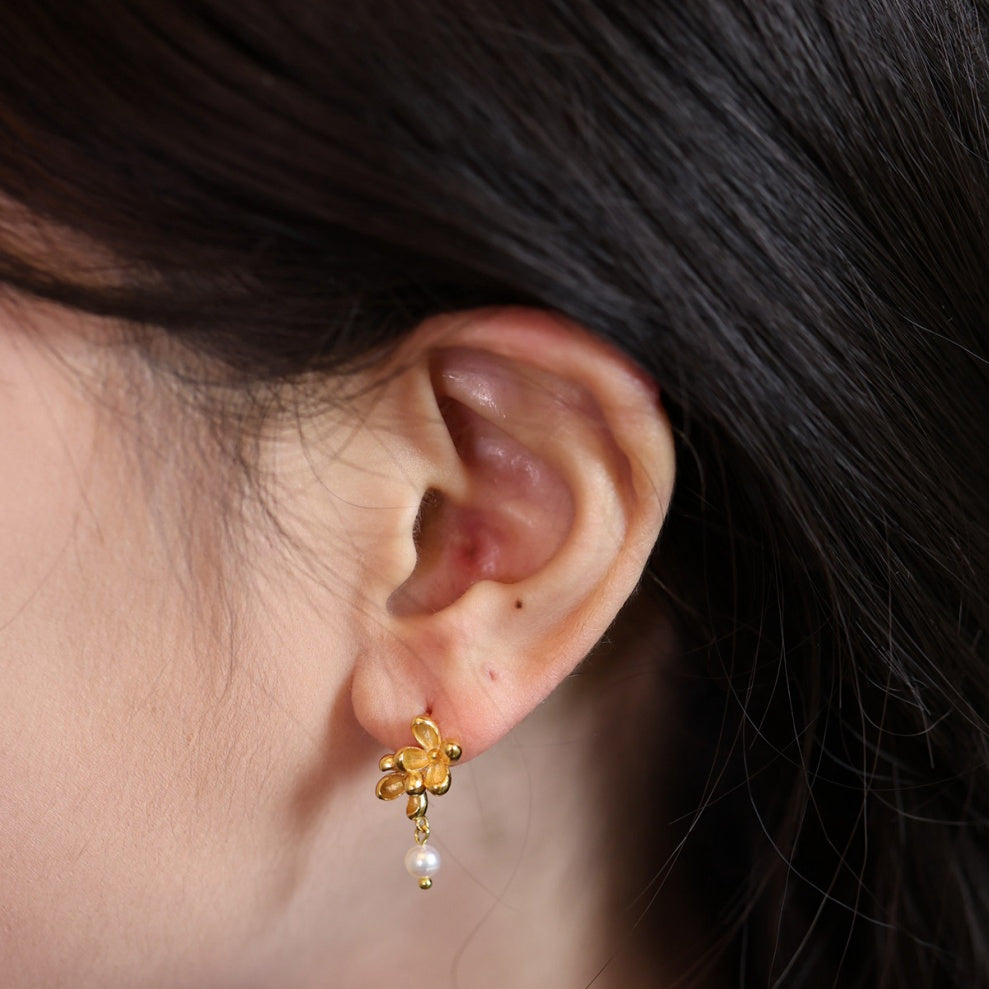 Model wearing dainty matte silver blossom earrings with a dangling natural freshwater pearl, 2.0cm length