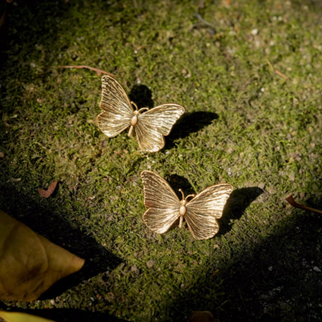 Gold butterfly earrings placed on green moss, nature-inspired jewelry gift idea.