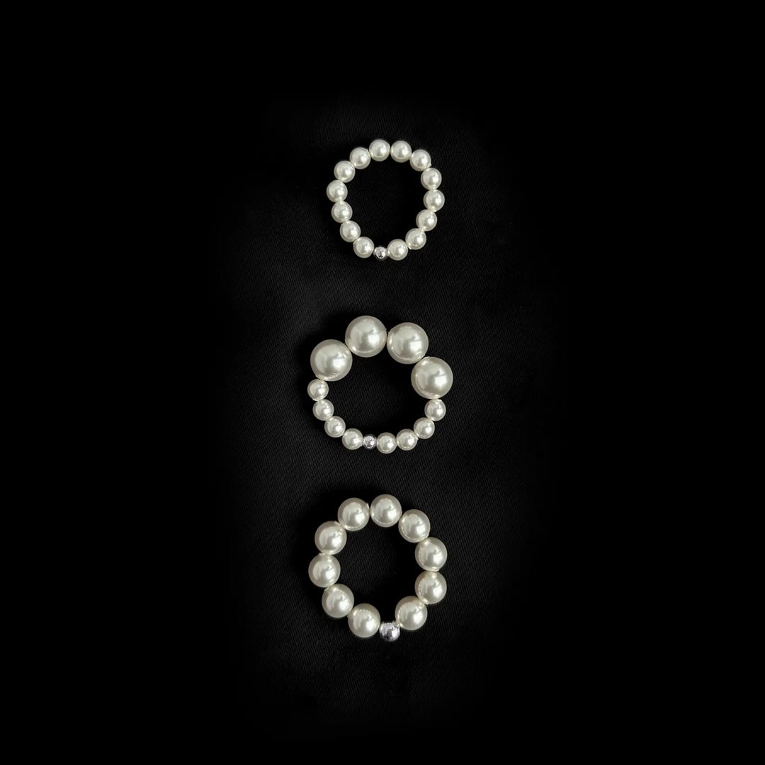 Three different sizes of white Swarovski pearl stretchy rings on black background.