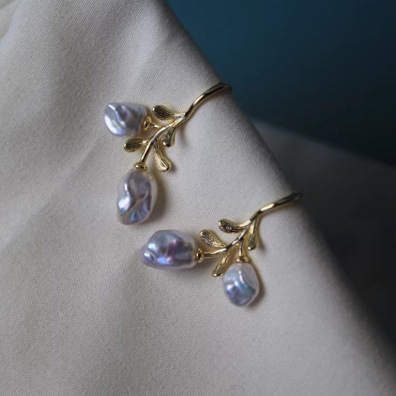 Natural baroque pearls with iridescent silver-blue glow attached to golden vine-shaped earring hooks.
