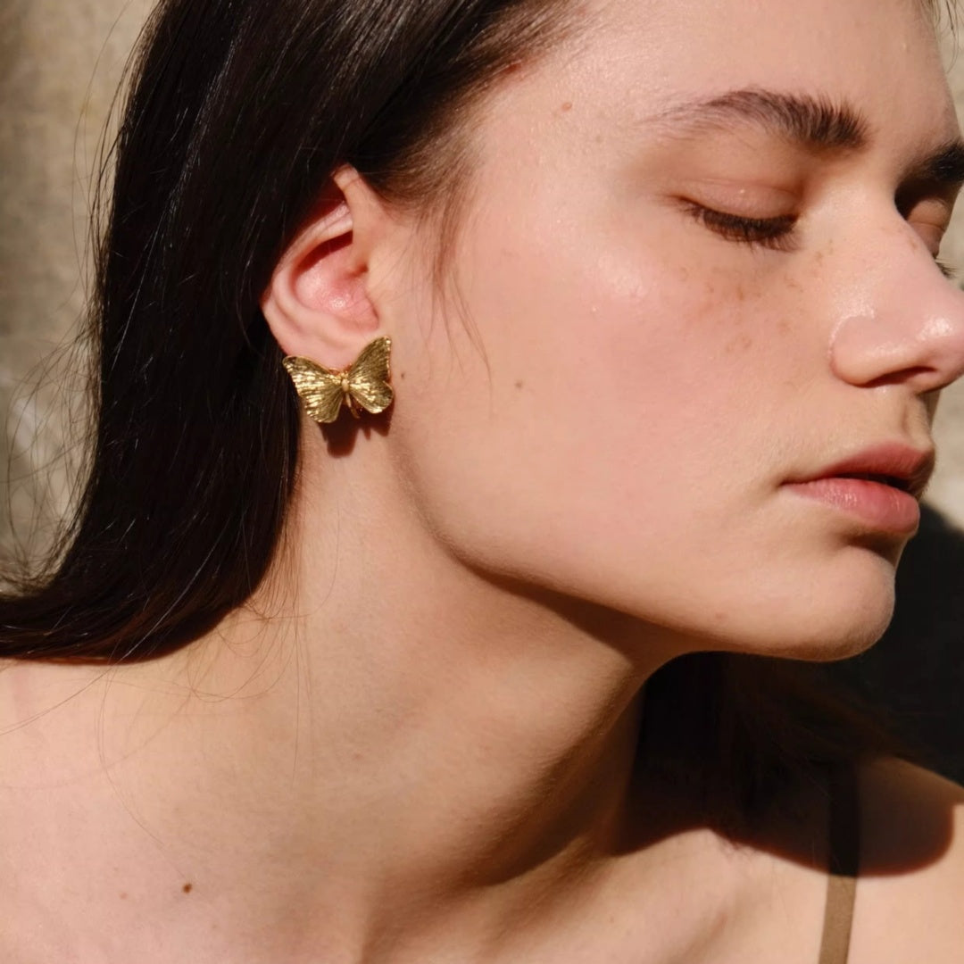 Close up of gold butterfly stud and ear cuff styling on model's ear.