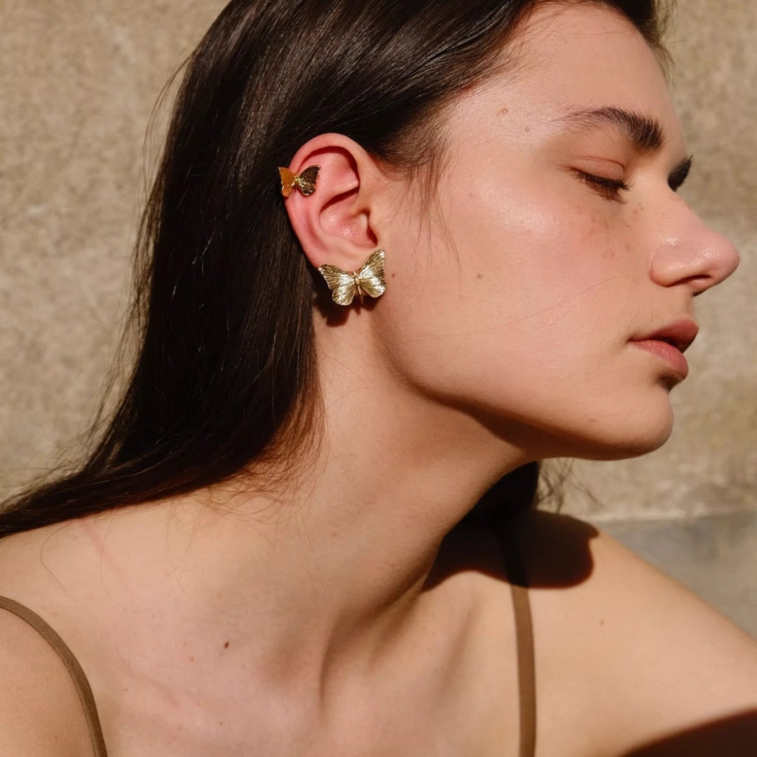 Woman wearing textured gold butterfly earrings in sunlight, vintage aesthetic.